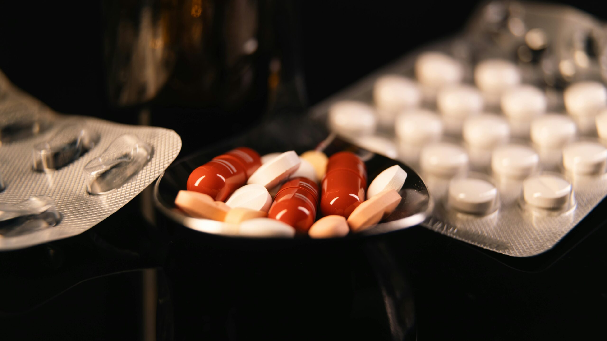 Close-up of assorted pharmaceutical pills in blister packs and a spoon on a dark background.